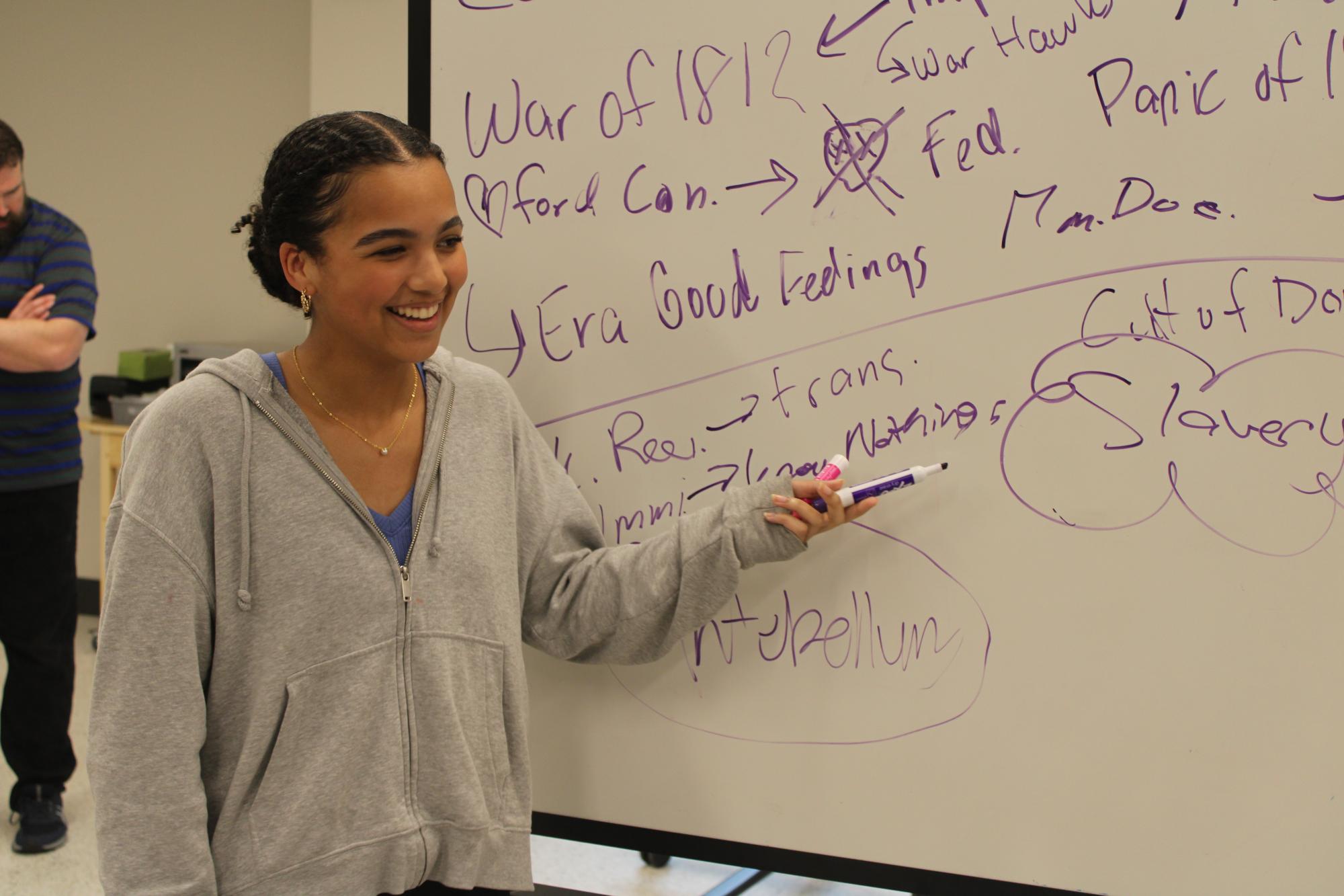 Boy talking in front of whiteboard to classmates